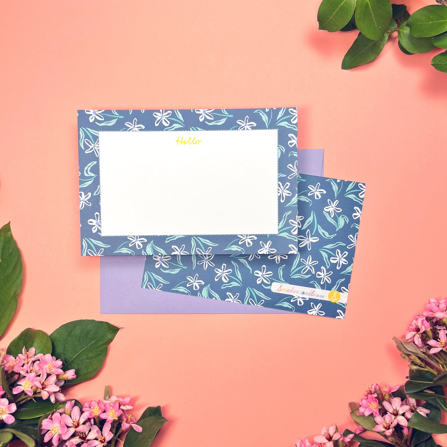 White dainty flower pattern on a blue background with teal and periwinkle accents. Stationery set of 10 with envelopes. Greeting says "Hello" in lime green. Shown with a lilac envelope.