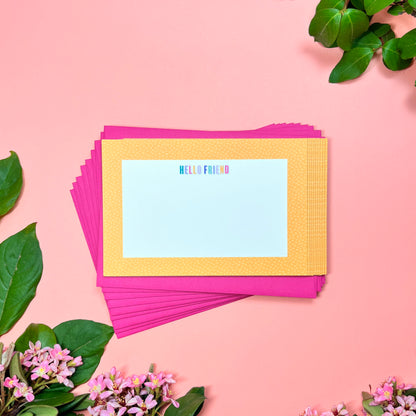 Cute yellow pebble spotted frame greeting card set of 10. Say "HELLO FRIEND" in a rainbow macaroon pastel way. Shown on a stack of magenta envelopes.
