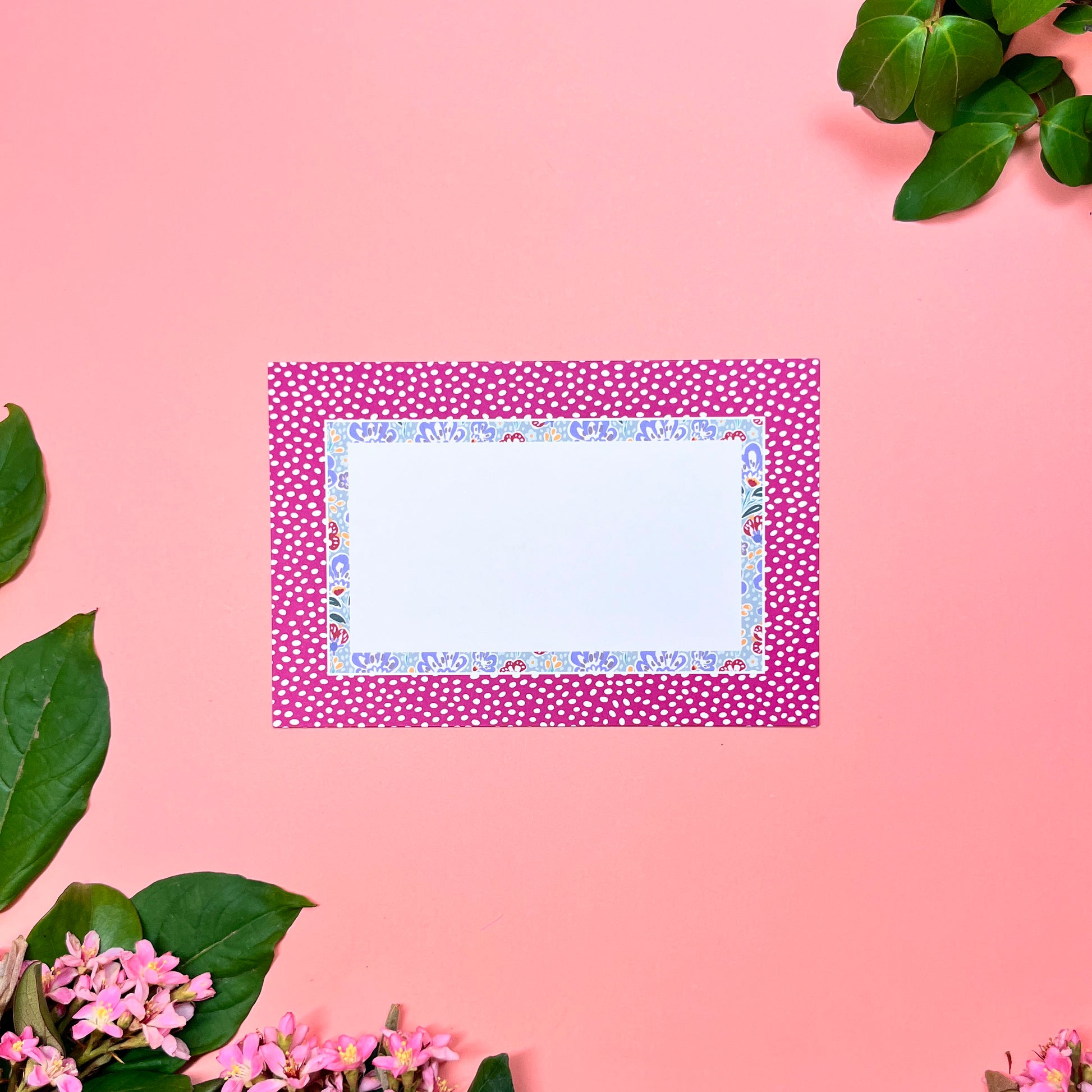 Flat greeting note card with a wine-pink polka dot cover on a pink background with green leaves and flowers.